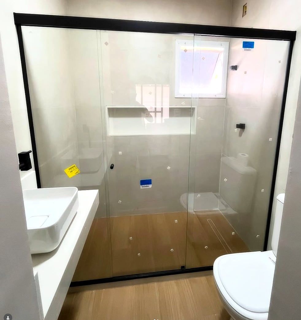 Box de banheiro em vidro temperado com perfil preto e porta de correr, em banheiro claro